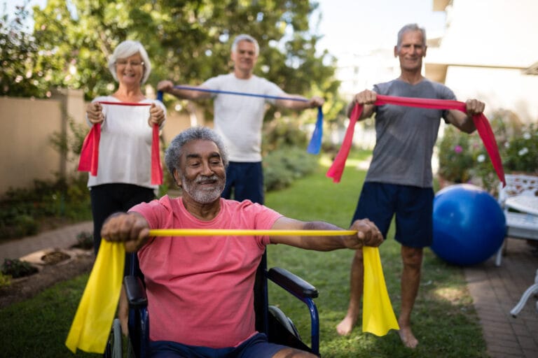 Physically impaired senior man holding ribbon with friends while exercising at park